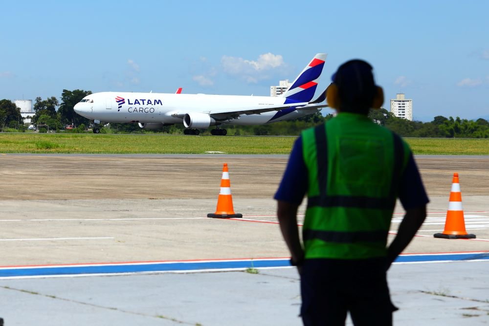 Aeronave cargueira em aeroporto com profissional de operações em primeiro plano, representando a cadeia logística da indústria aeronáutica e fábricas de aviões no Brasil.