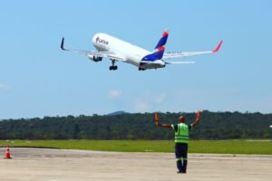 Un avión de carga despega mientras un profesional dirige las operaciones en la pista, simbolizando la expansión de las conexiones aéreas entre São José dos Campos y Estados Unidos y su competitividad en los negocios globales.