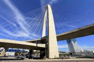 Ponte estaiada em São José dos Campos, cidade que integra o ecossistema de inovação no Brasil, com torre de concreto e cabos de sustentação contra o céu azul, tendo ao fundo prédios comerciais da região das Colinas.