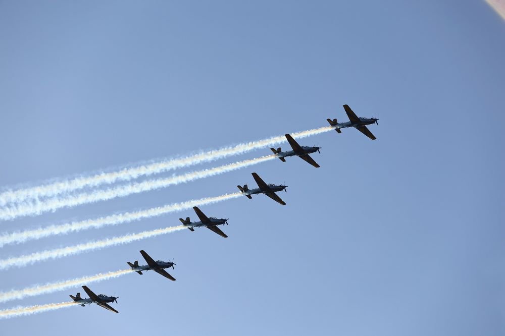 Sete aeronaves militares brasileiras em formação de voo com rastros de fumaça, representando a tradição da engenharia e das empresas aeroespaciais no Brasil.