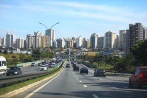 Rodovia expressa movimentada em São José dos Campos, com skyline de prédios residenciais ao fundo, representando a infraestrutura urbana que sustenta o crescimento de startups em São José dos Campos.